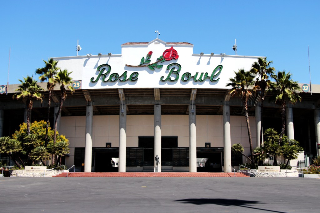 The entrance of the Rose Bowl stadium, adorned with a large "Rose Bowl" sign and rose logo, with palm trees on either side.