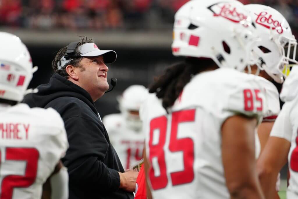 Jason Eck, wearing a New Mexico visor, looks up with players around him on the sideline