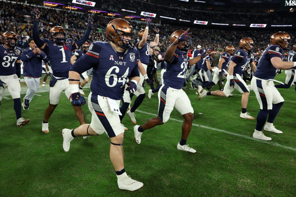 Navy football players run onto the field, some with arms raised