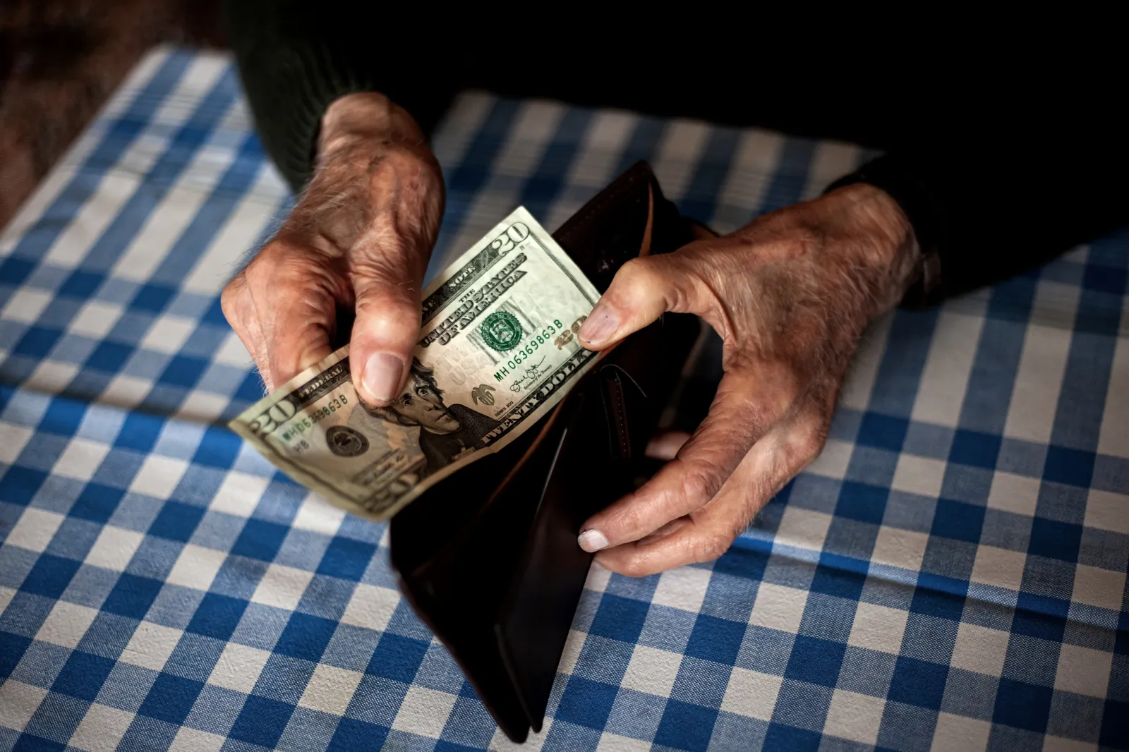 Stock image: A man holds a wallet and a $10 note at a table with a checkered tablecloth.