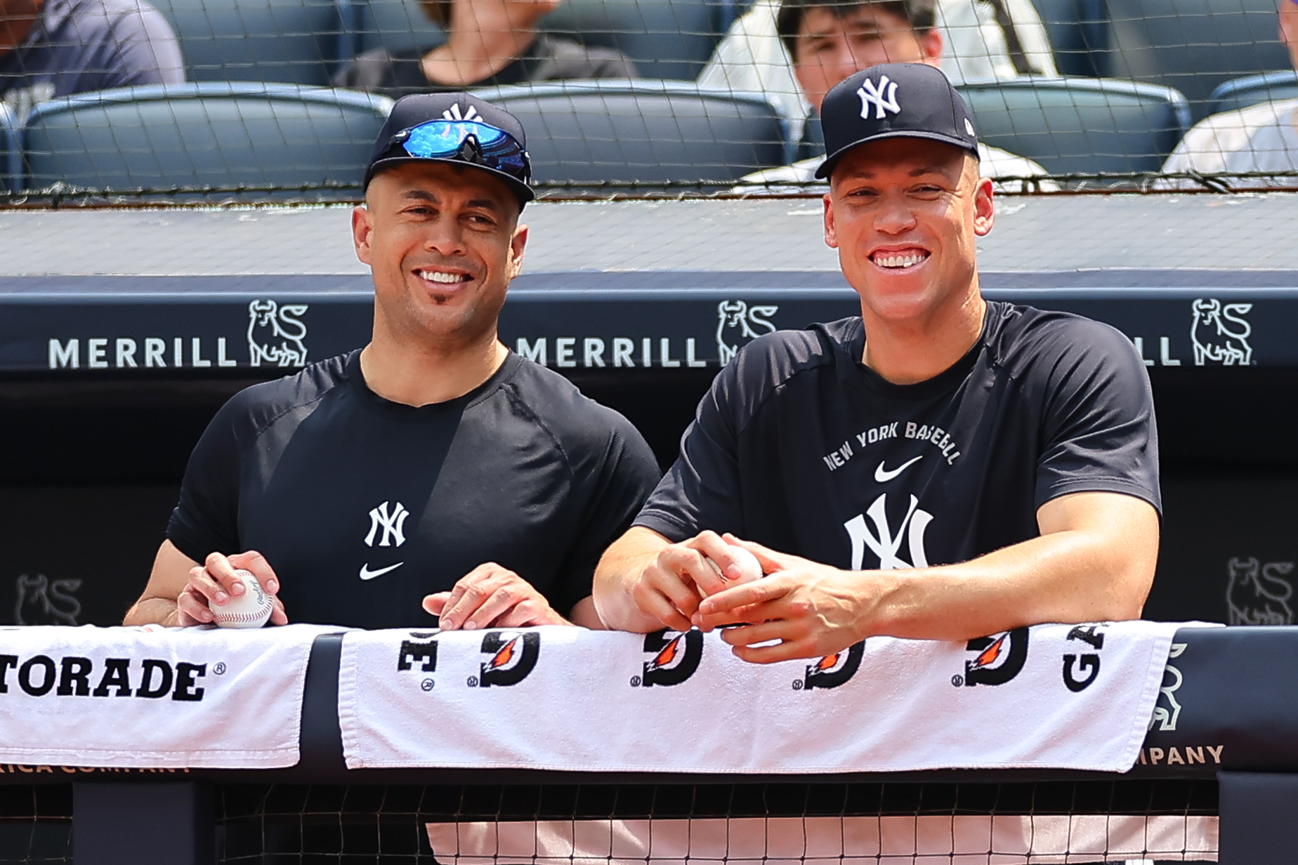Giancarlo Stanton, left, and Aaron Judge stand next to each other at the dugout railing, smiling.