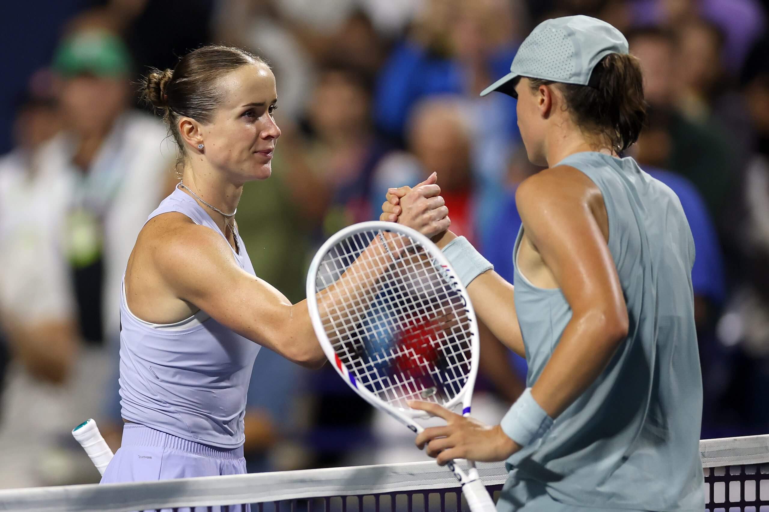 Elina Svitolina and Iga Świątek, with ballcap on, shake hands at the net.
