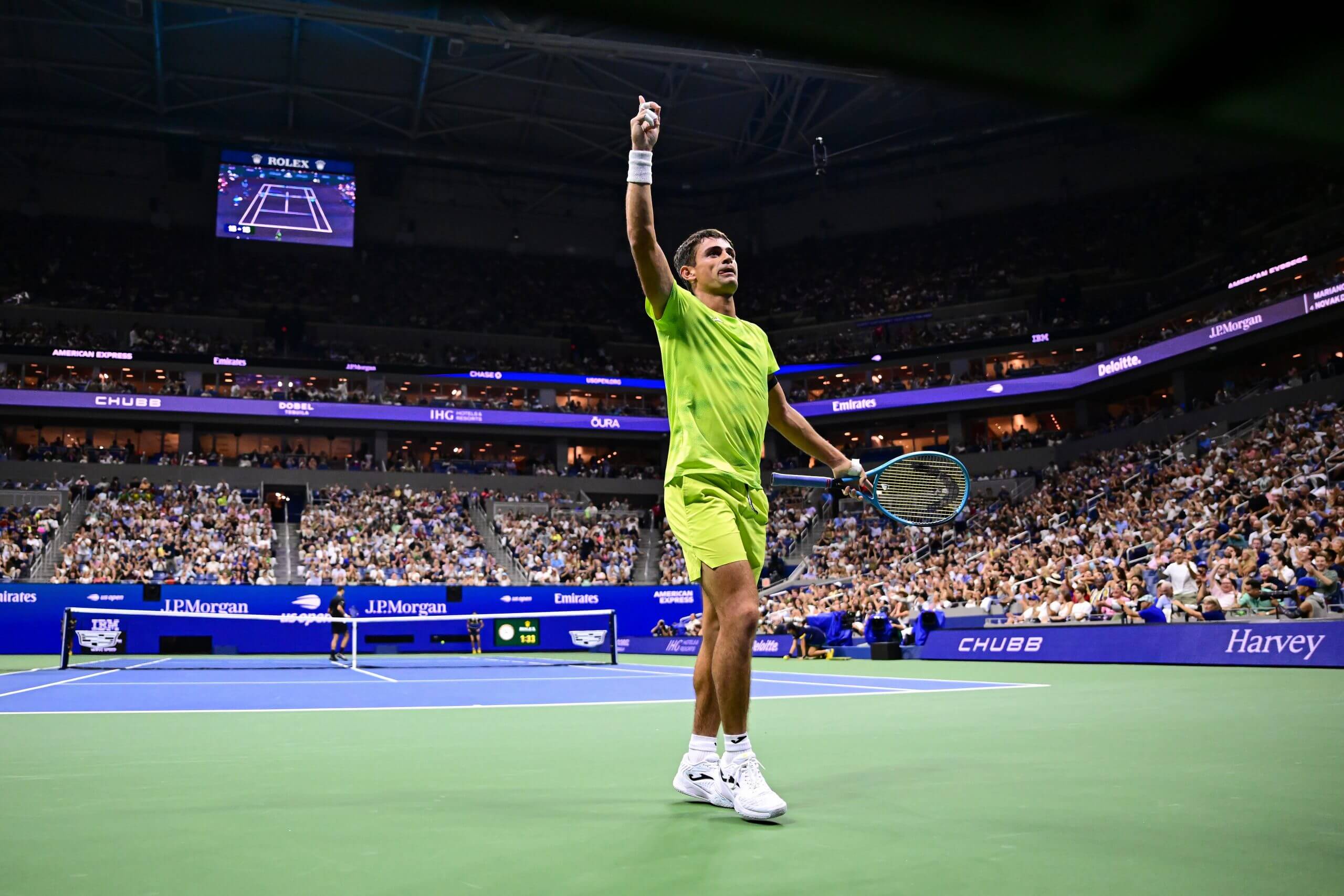 Mariano Navone points to the sky to acknowledge the crowd on a full tennis court.