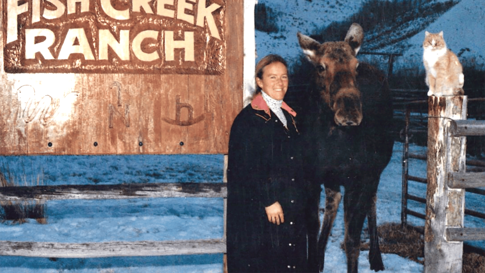 Pamela Chrisman stands with one of her longtime moose visitors outside the Fish Creek Ranch sign.