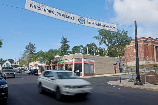 A car drives under the banner asking to 'finish Norwood Hospital', just down the street from the abandoned worksite at Norwood Hospital. (staff photo by Stuart Cahill/Boston Herald)