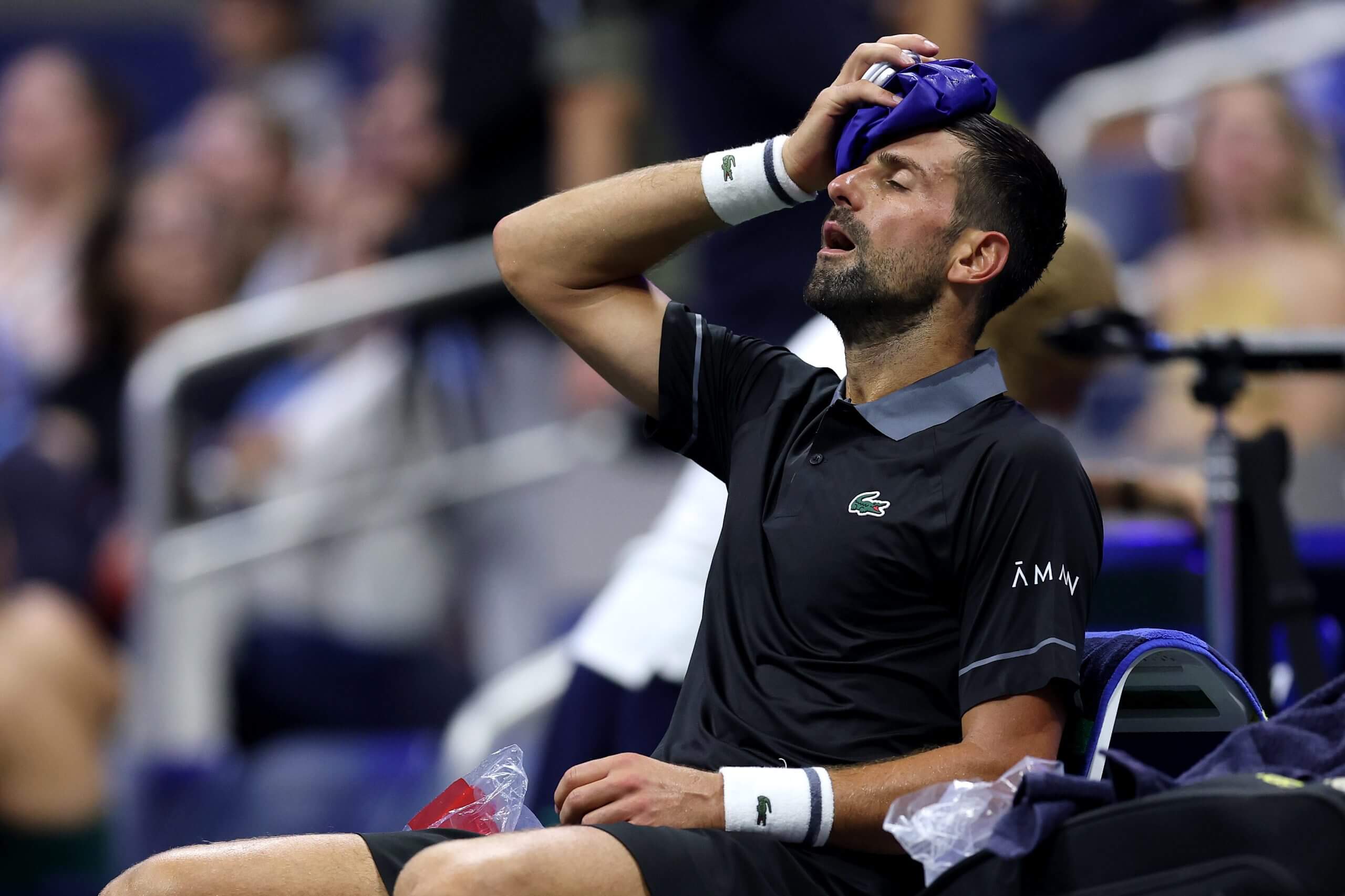 Novak Djokovic puts an ice pack on his head as he sits on a chair.