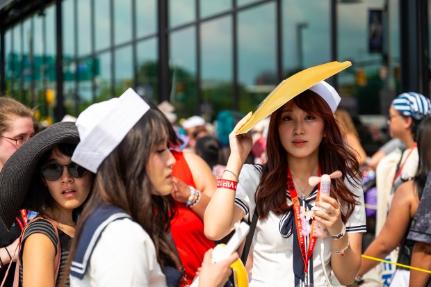 Corina Suherman, 21, shields herself from the sun and uses a personal fan while waiting in line for the BTS concert at M&T Bank Stadium. Suherman traveled from California to see BTS perform in Baltimore, the 16th stop of the group's "Arirang" World Tour. (Ryan Bowie/Staff)