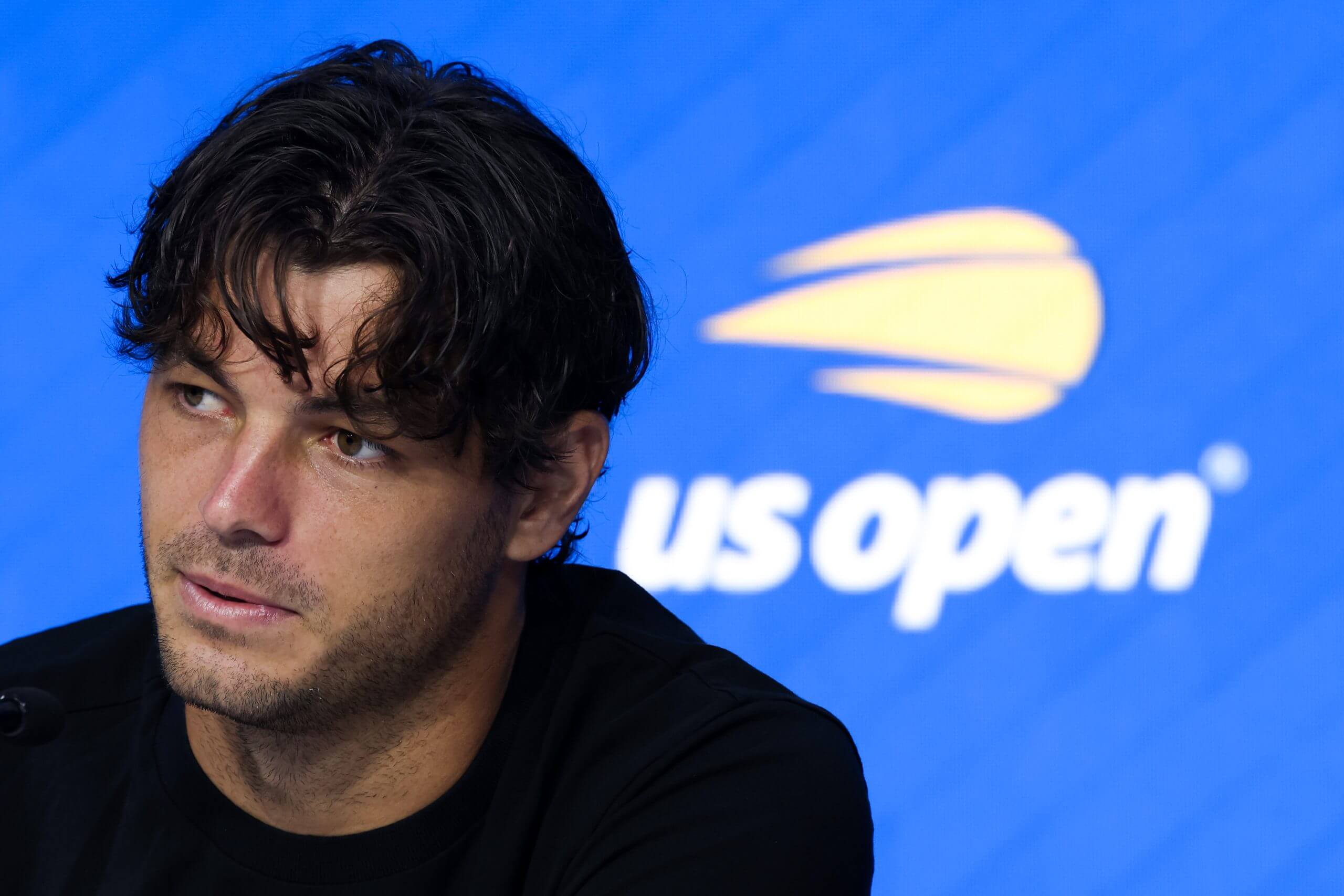 Taylor Fritz looks on in front of a U.S. Open logo.