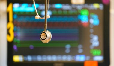 A stethoscope hangs in front of a medical monitor displaying patient vital signs with colorful graphs and numbers.