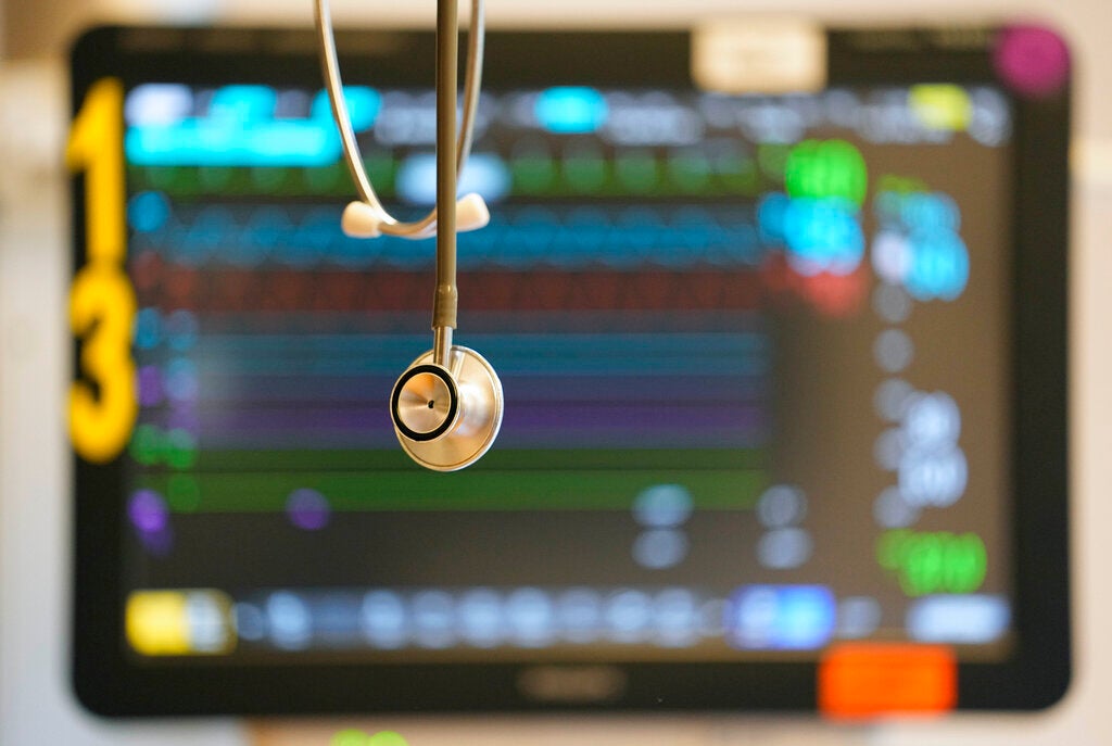 A stethoscope hangs in front of a medical monitor displaying patient vital signs with colorful graphs and numbers.