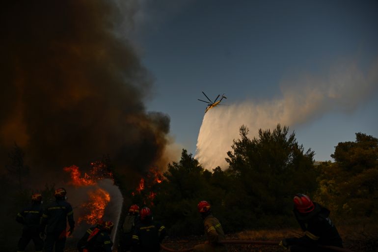 A firefighting helicopter drops water over a smoke-filled forest during a wildfire near Porto Germeno, northwest of Athens, Greece, Sunday, Aug. 2, 2026. (AP Photo/Michael Varaklas)