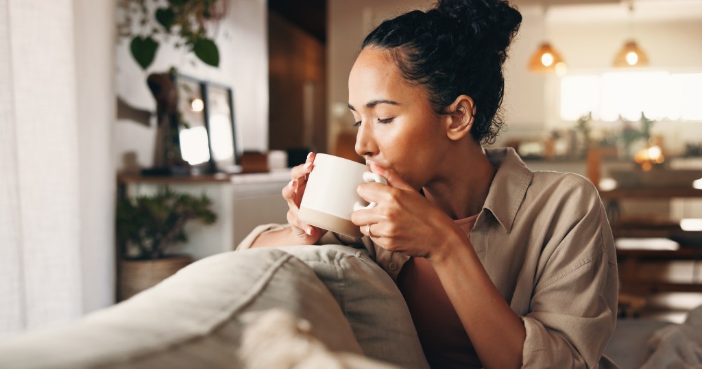 A woman relaxing on a sofa and drinking coffee from a mug.