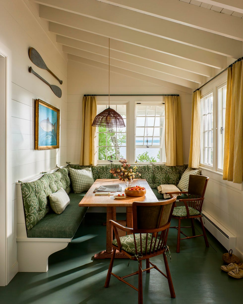 Cozy breakfast nook with green patterned seating, wooden table, floral centerpiece, and large windows offering natural light. Cozy breakfast nook with green patterned seating, wooden table, floral centerpiece, and large windows offering natural light.