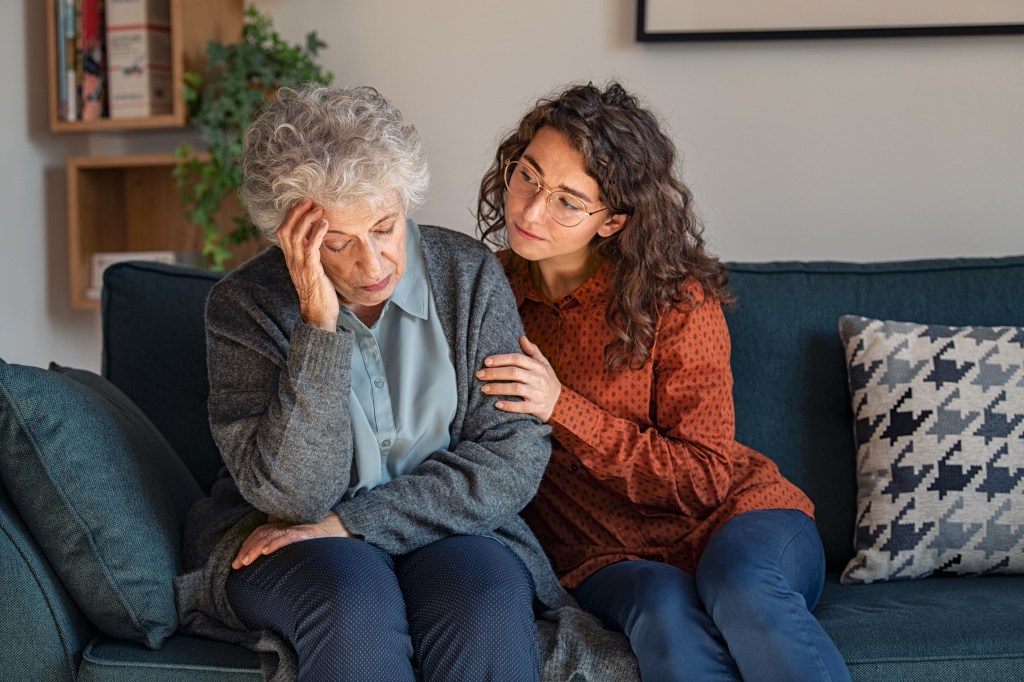 A younger woman comforting an older woman who is sitting with her head in her hand.