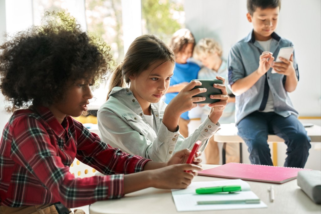 Diverse multiethnic kids students using smartphones in classroom.