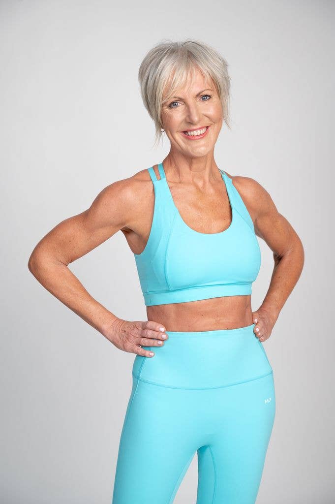 older woman smiling with her hands on her hips in aqua blue activewear