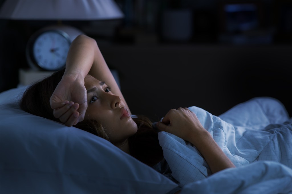 A young Asian woman lying in bed, looking worried and unable to sleep.