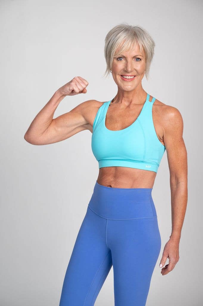 older woman flexing her muscles in mismatched blue activewear