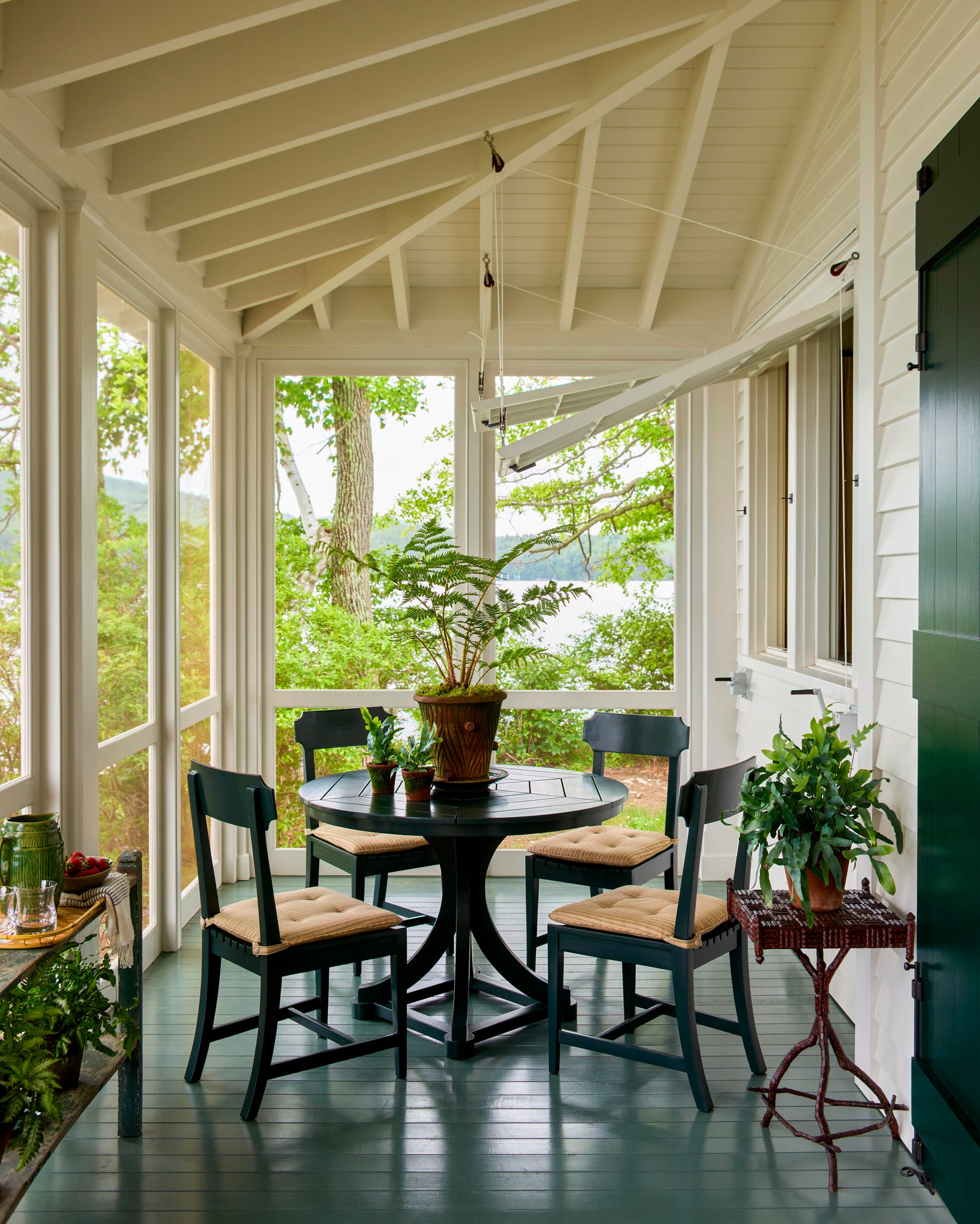 A cozy screened porch with a round table, four chairs, potted plants, and views of the lake.