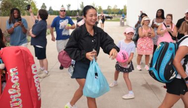 A tennis player in black greets fans