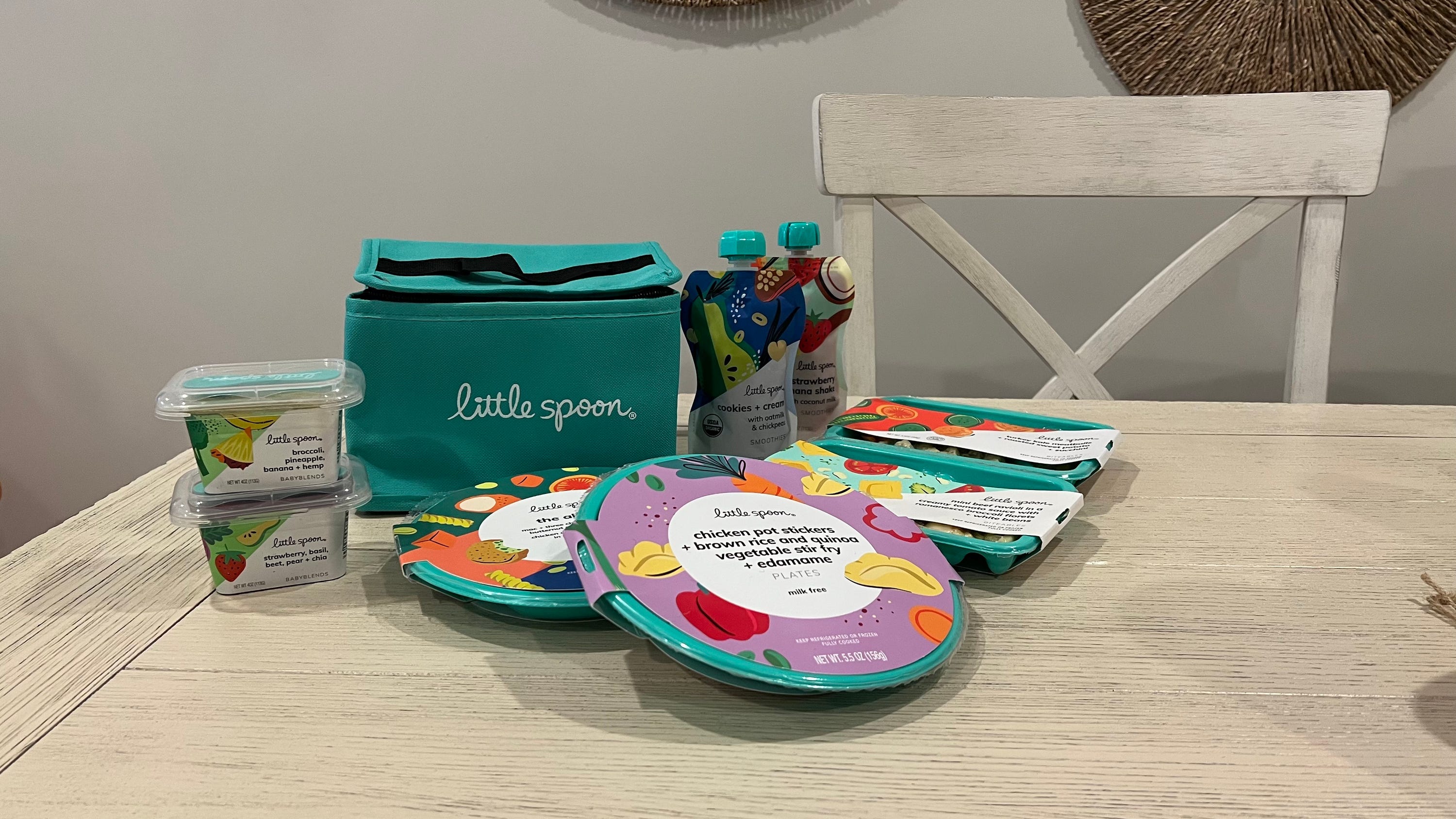 Assorted baby food containers and plates from Little Spoon on a wooden table.