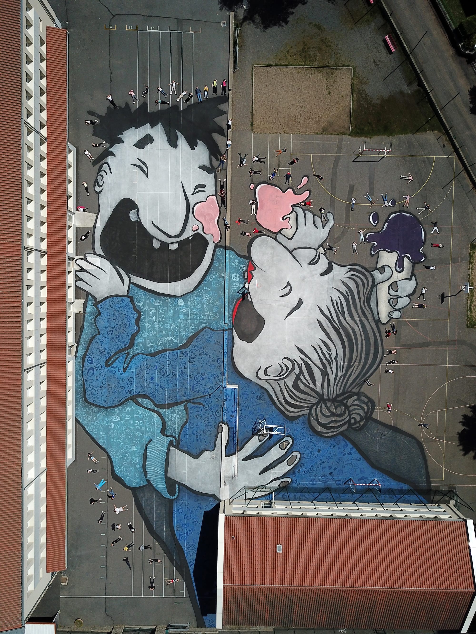 an aerial view of a large mural by Ella & Pitr on the ground of a public square featuring a cartoonish pair of laughing figures
