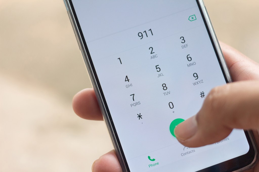 A hand holding a smartphone with "911" dialed on the screen.
