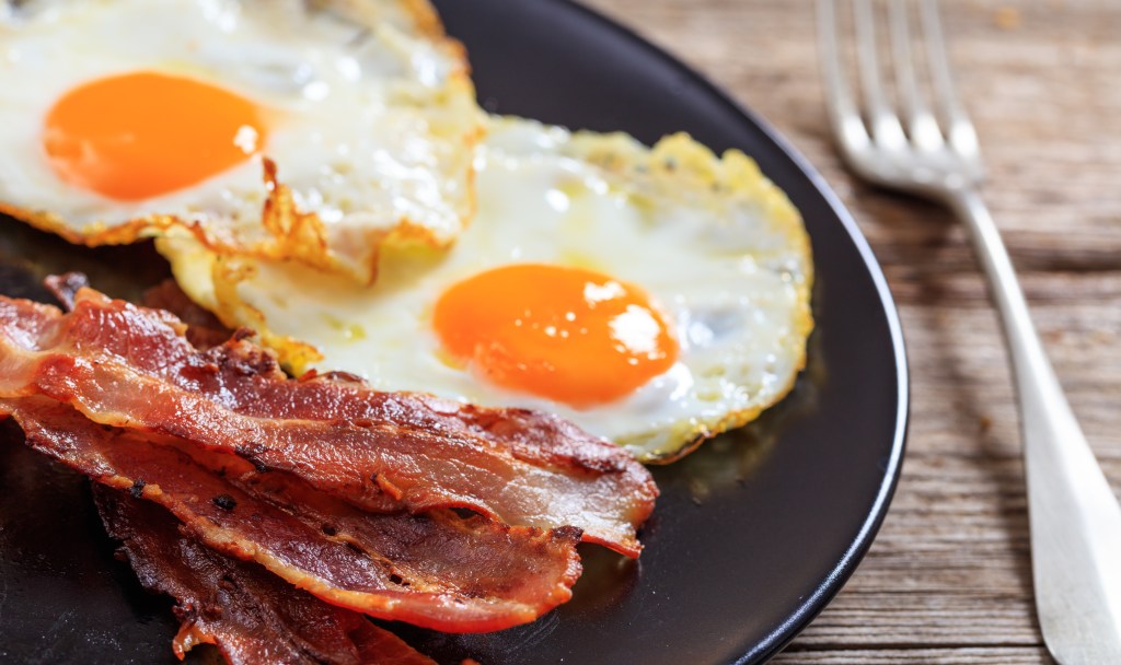 Plate of fried eggs and bacon on a wooden surface.