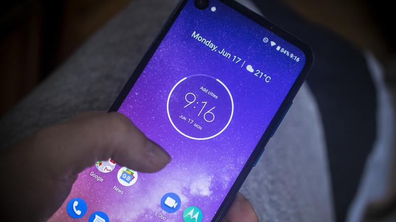 Person using a Motorola phone with the home screen visible.