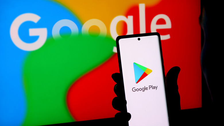A hand holds a phone displaying the Google Play logo with a large Google logo visible in the background.