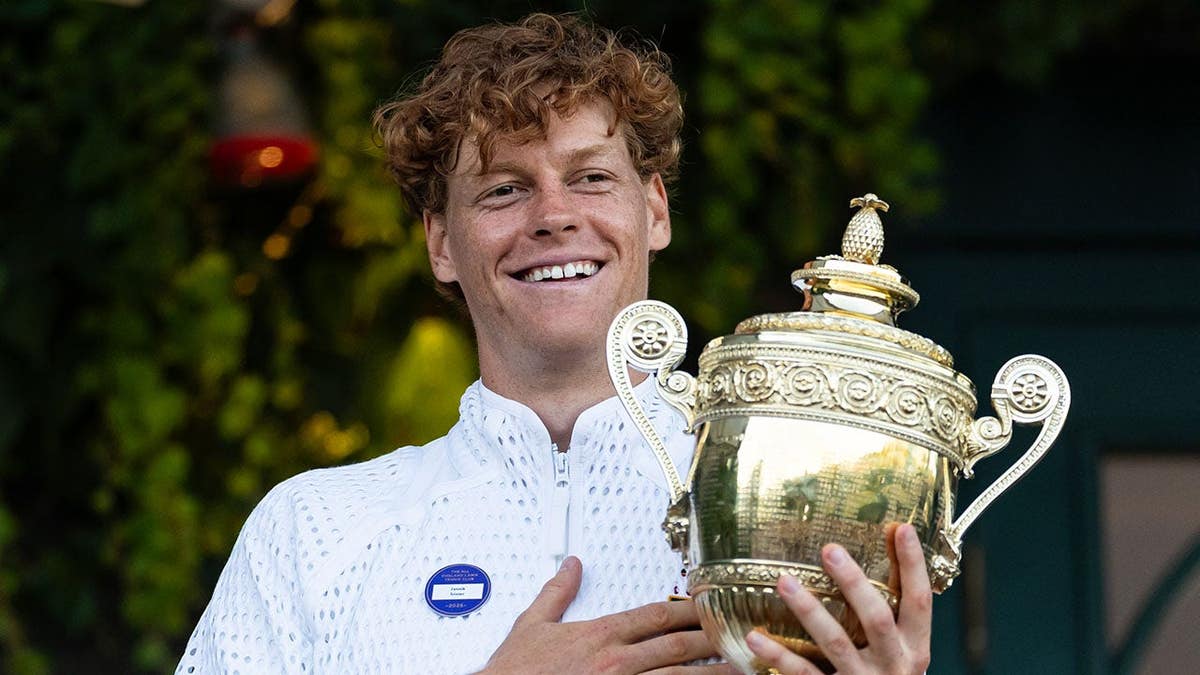 Jannik Sinner holds the Gentlemen's Singles Trophy over the Royal Box balcony.