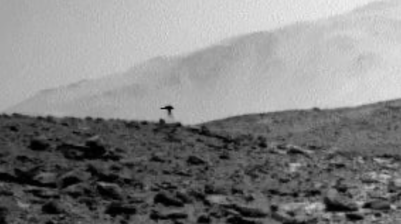 Fuzzy, black and white view of a rocky hill, with a dark jellyfish-like shape on top of it.