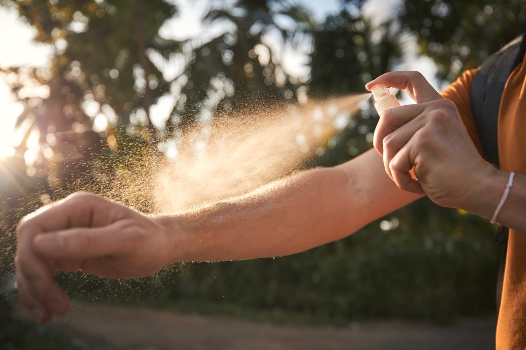 Man spraying insect repellent on his arm outdoors to prevent mosquito bites.