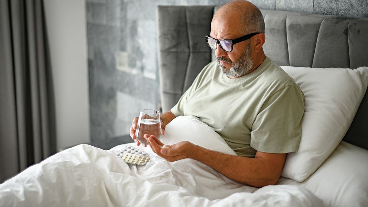 Man takes medication in bedroom interior.