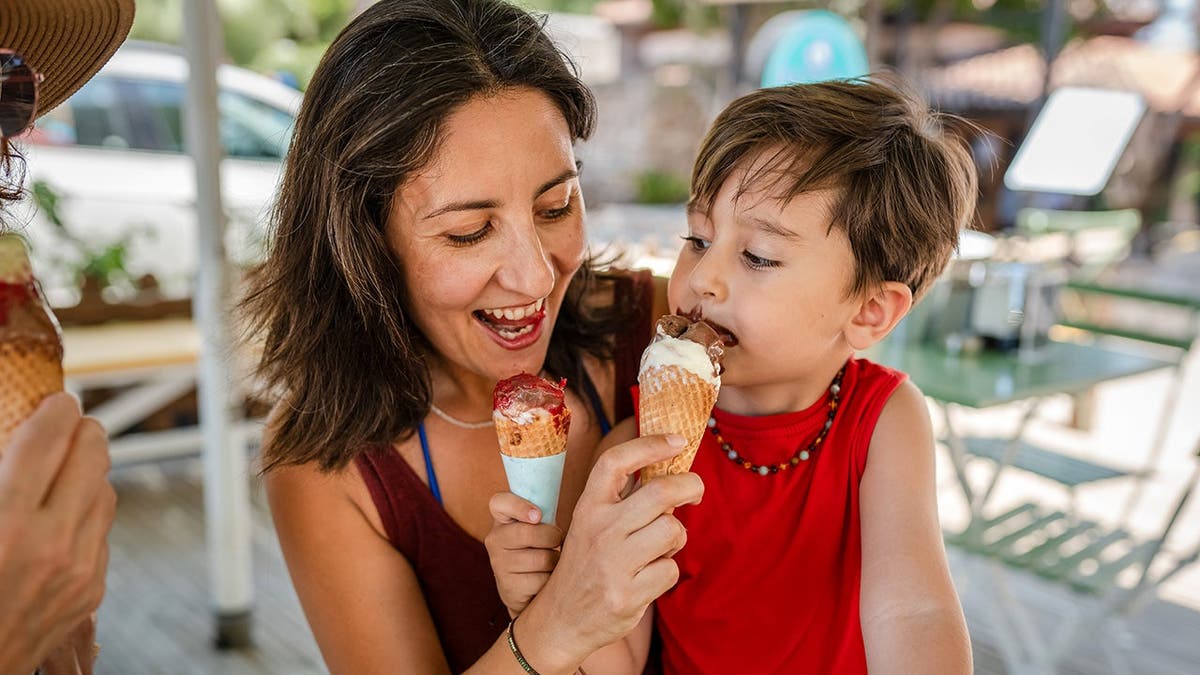 A woman feeds an ice-cream cone to a child.