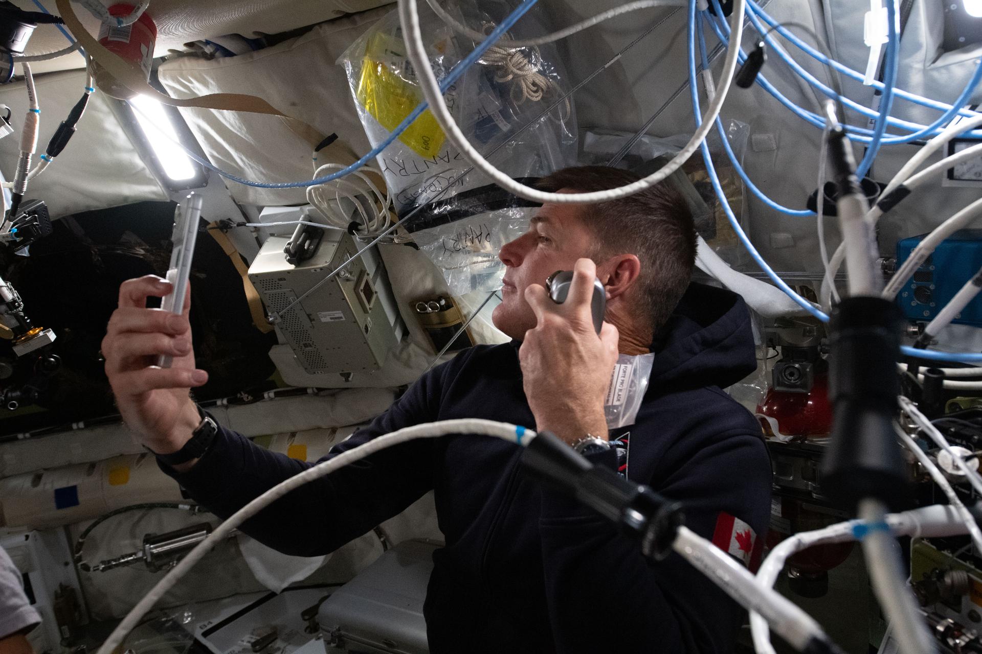 A man holding a shaving apparatus in his hand and using his phone camera as a mirror.