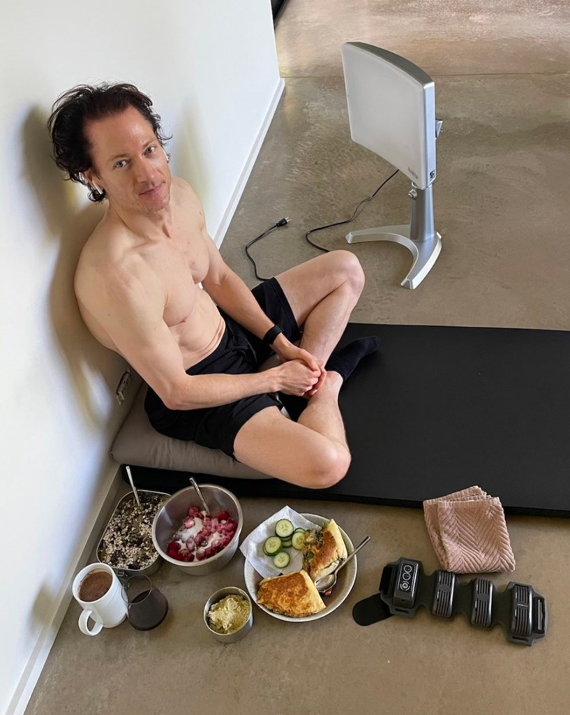 Bryan Johnson sits next to his meals for the day, a light therapy lamp, and a massage mat.