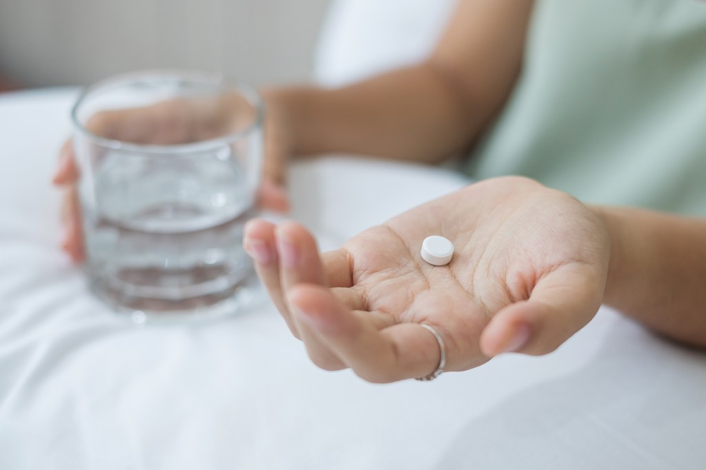Close-up of a person holding a white pill in one hand and a glass of water in the other.