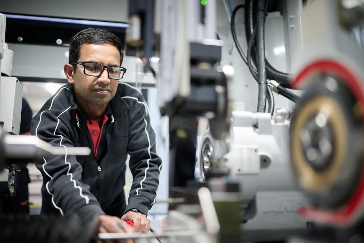 A worker wearing a black zipper is working on a machine inside a factory.