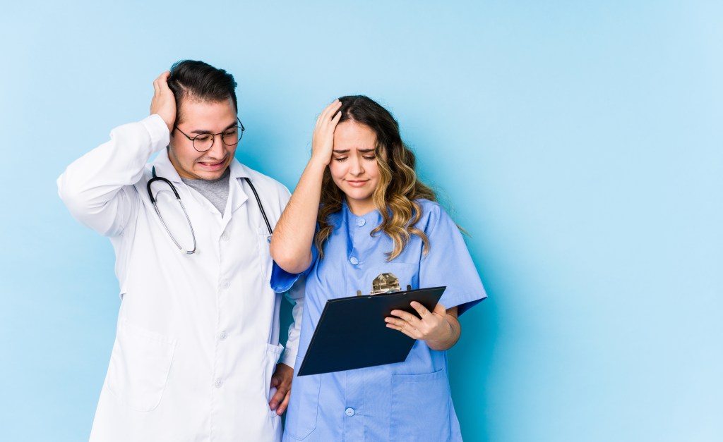 Two doctors, a man and a woman, holding their heads in frustration.