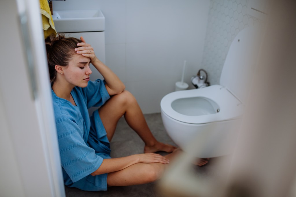 Young sick woman sitting on the floor near a toilet.