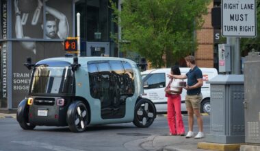 Pedestrians watch as a Zoox robotaxi passes along East Fifth Street in Austin.