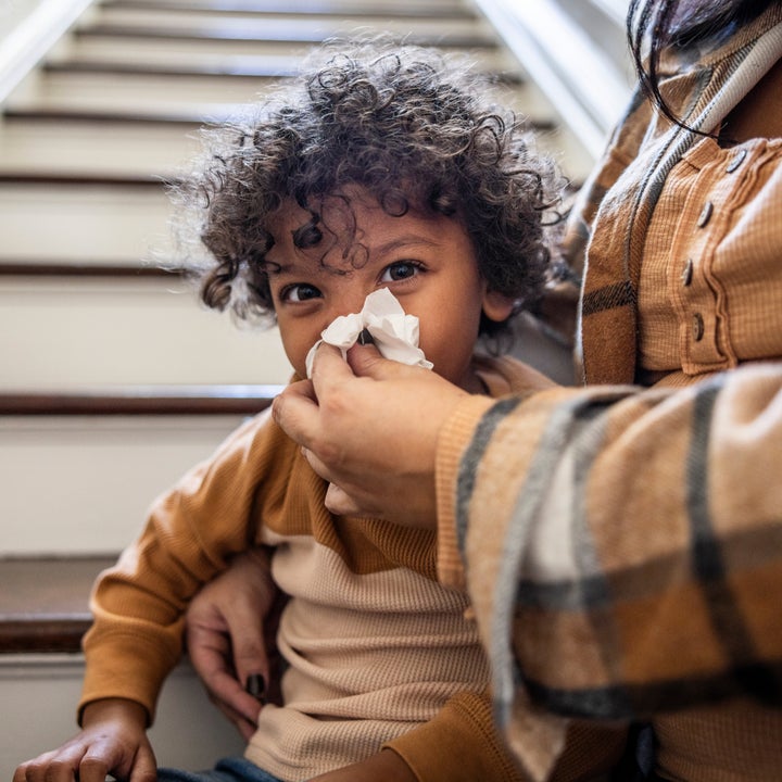 Child sitting on stairs is gently having their nose wiped with a tissue by an adult, showing a caring moment