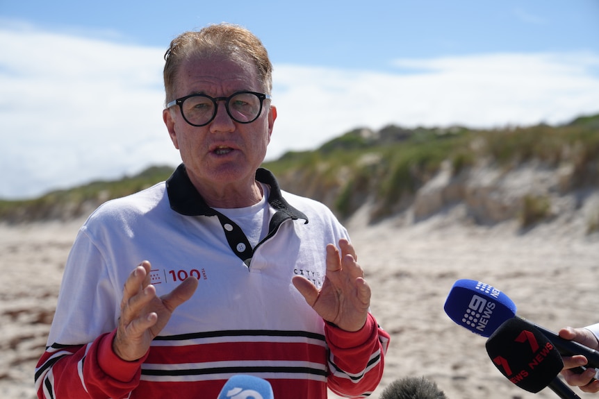 A head and shoulders shot of Town of Cambridge Mayor Gary Mack speaking during a media interview standing on City Beach..
