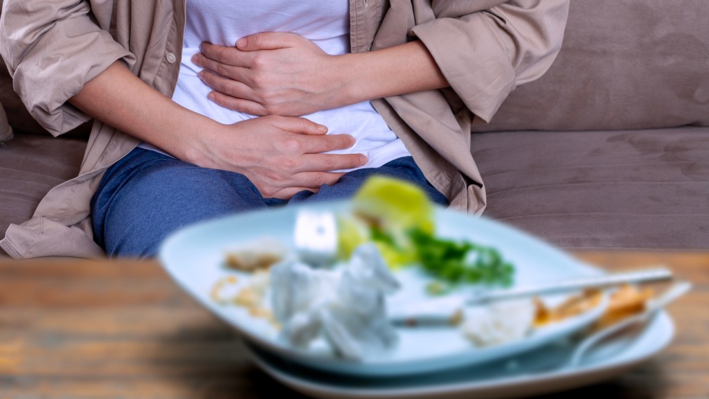 A woman clutches her stomach in pain after food poisoning, with a dirty plate of food in the foreground.