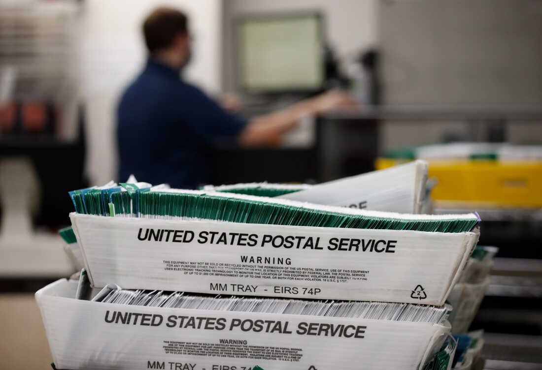 Election workers stack ballots that were picked up at a U.S. Postal Service office. The bin says United States Postal Service on the side.