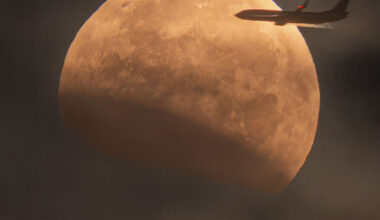 The Moon is seen in front of clouds but with part
of its lower left being unusually dark. On the upper 
right, a foreground airplane appears flying into the disk of
the Moon.  
Please see the explanation for more detailed information.