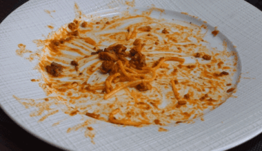 A diner places a knife and fork on a plate of nearly finished spaghetti.