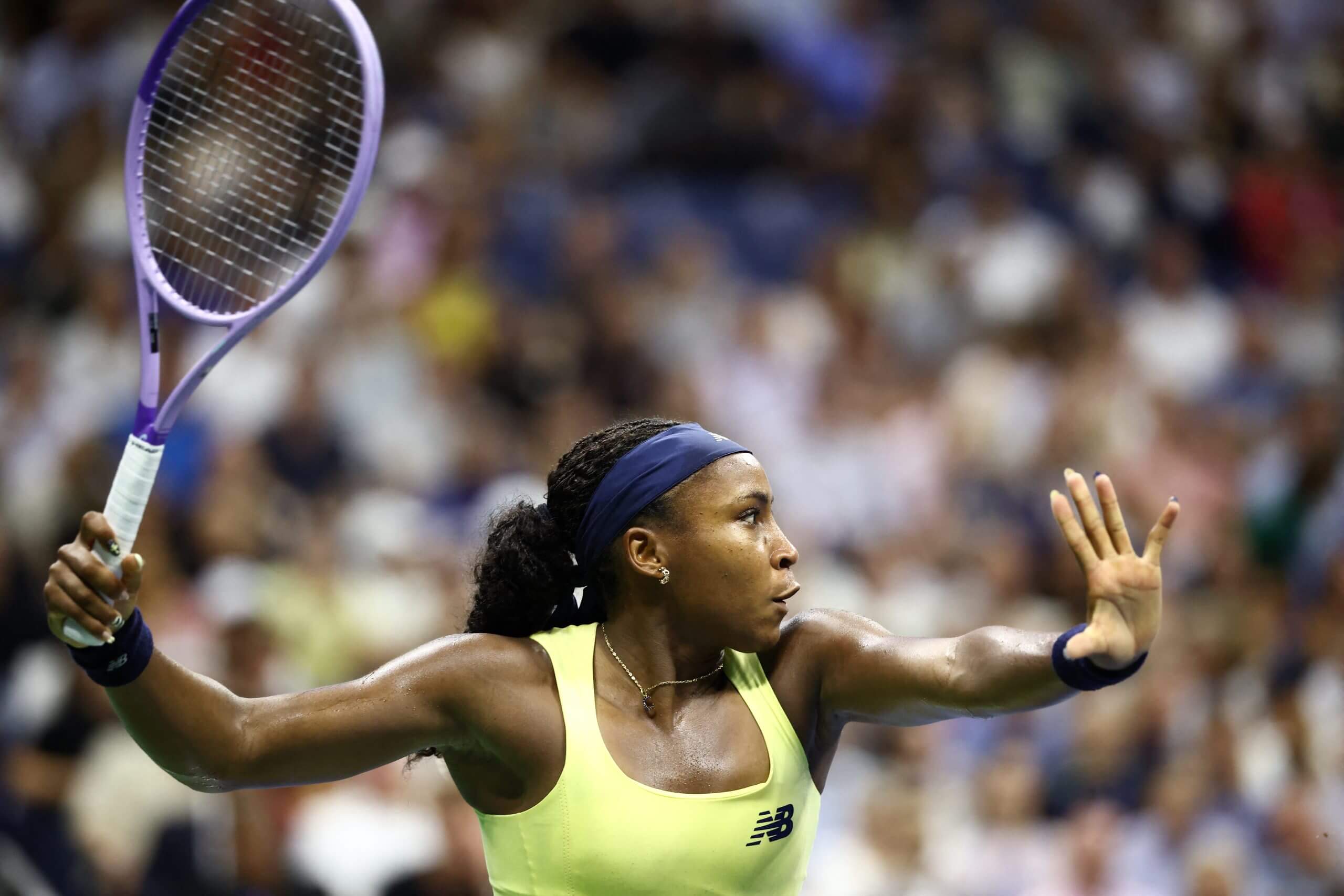 Coco Gauff prepares to hit a forehand wearing a yellow tennis outfit with her purple racket pointing upward.