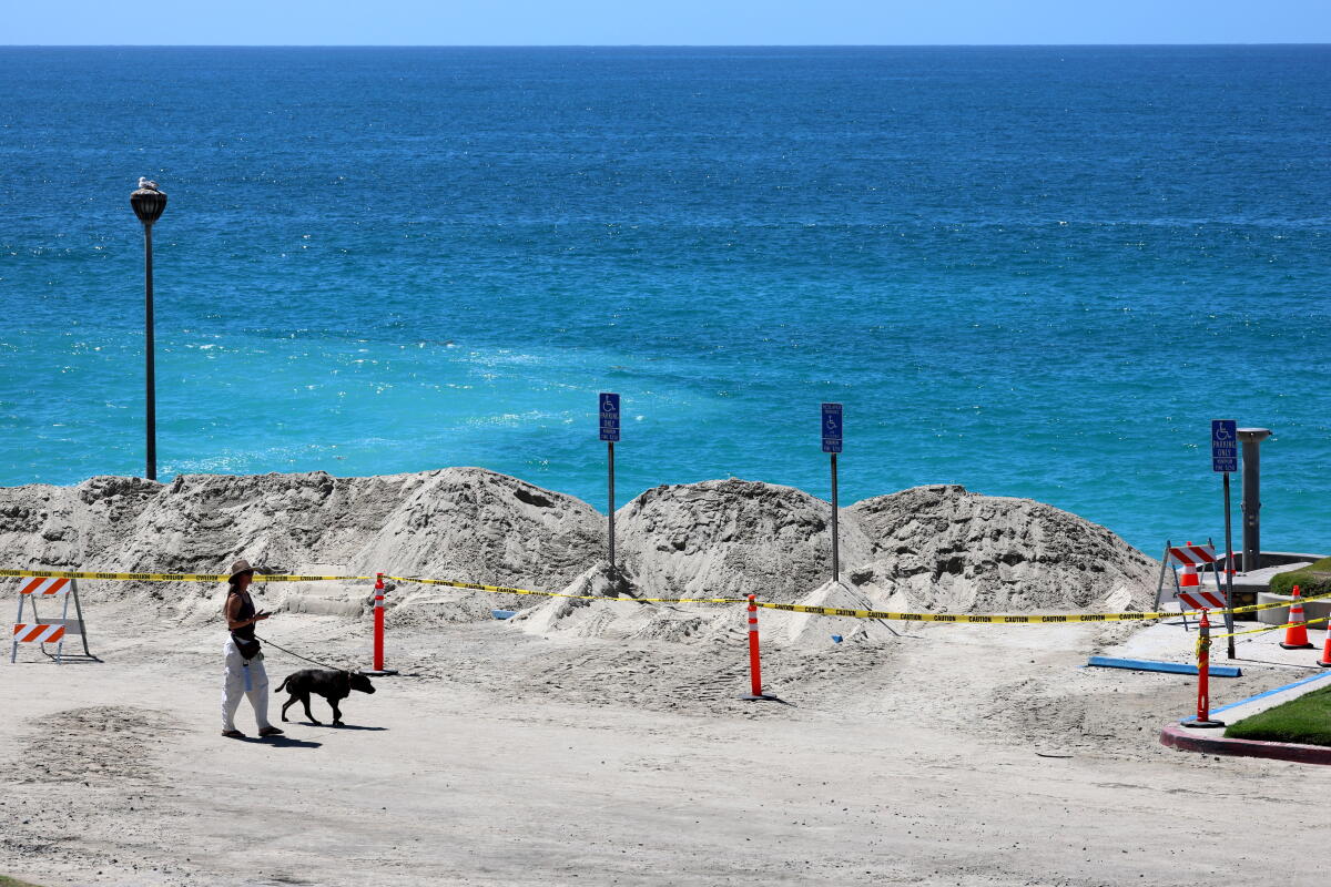 A person walks their dog through a closed parking lot and past a recently built sand berm at Aliso Beach